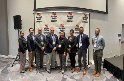 Board and Staff stand in front of a maryland society of surveyors sign at conference