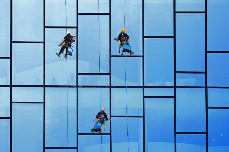 Three workers suspended from ropes clean windows on the outside of a building.