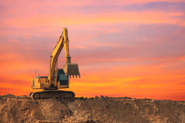 An excavator preparing to dig in dirt against a pink, orange, and yellow sky
