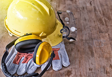 Hard hat, safety goggles, earmuffs, and safety gloves on wooden floor
