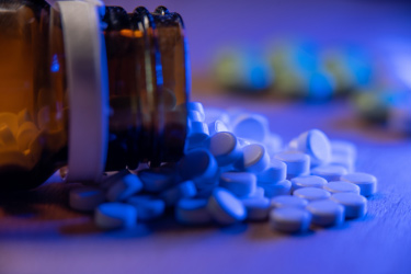 A bottle of pills on its side with lots of round, white pills spilling out of the bottle.